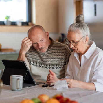 Senior couple sitting at the kitchen table looking at digital tablet and recalculating their expenses.
